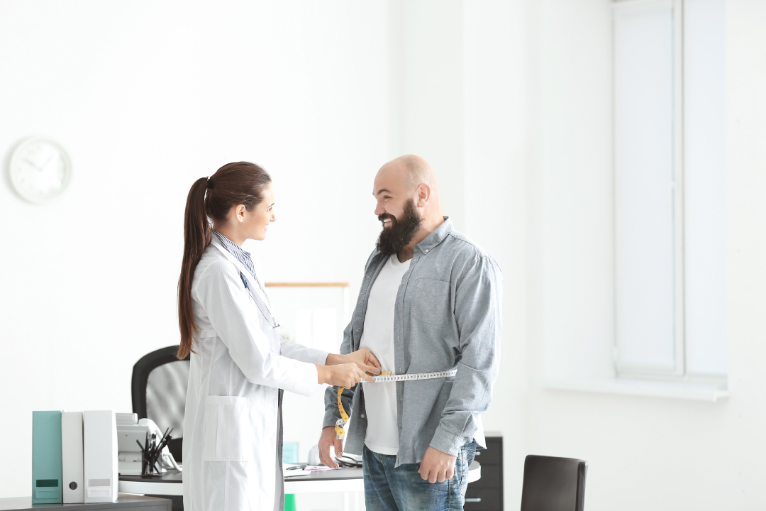 A doctor measures a man’s waistline in a bright medical office, showcasing progress from Bioidentical Hormone Replacement Therapy weight loss.